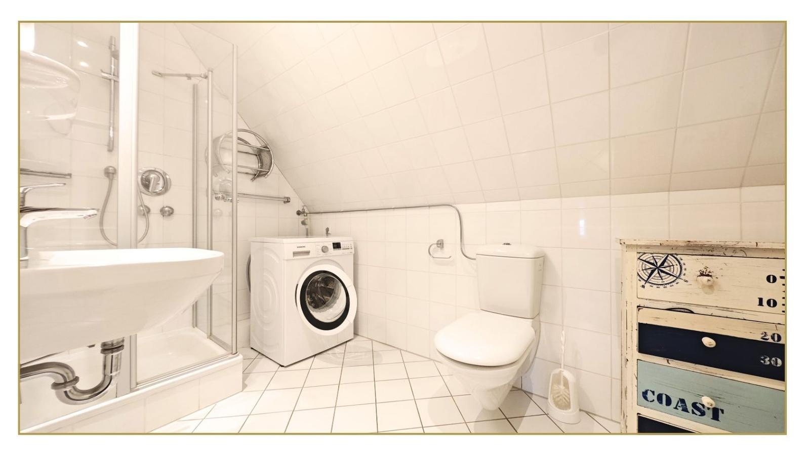 Badezimmer mit Dusche, Waschmaschine und Toilette. Holzschrank mit Nautikmotiven.