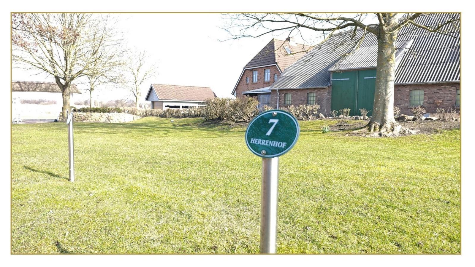 Grüner Hofzaun mit Schild 7 HERRENHOF. Im Hintergrund steht ein traditionelles Bauernhaus.