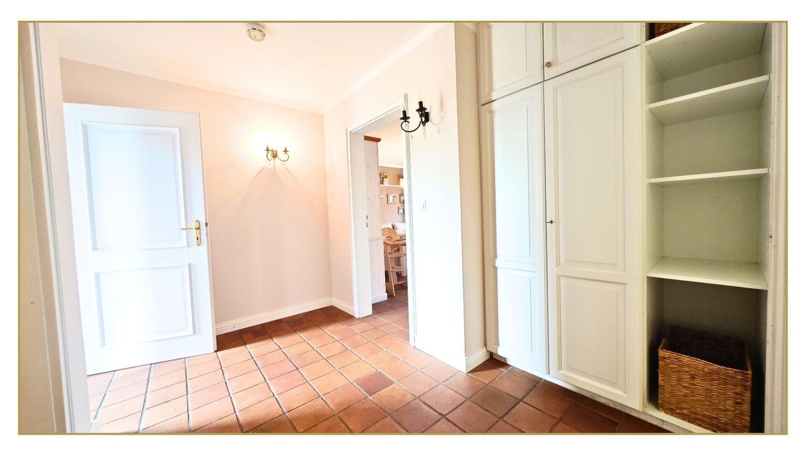 Hausflur mit weißen Schränken und Terrakottbodenfliesen. Durchgang zur Küche.