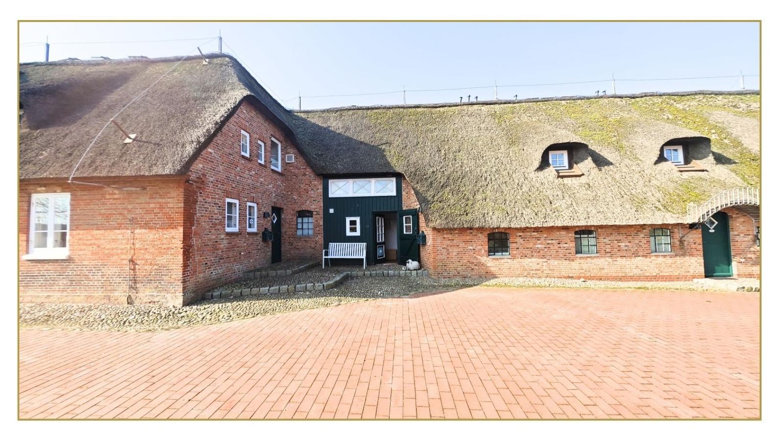 Haus mit Strohdach und Backsteinfassade, Vorgarten mit Steinplatten und weiße Bank.