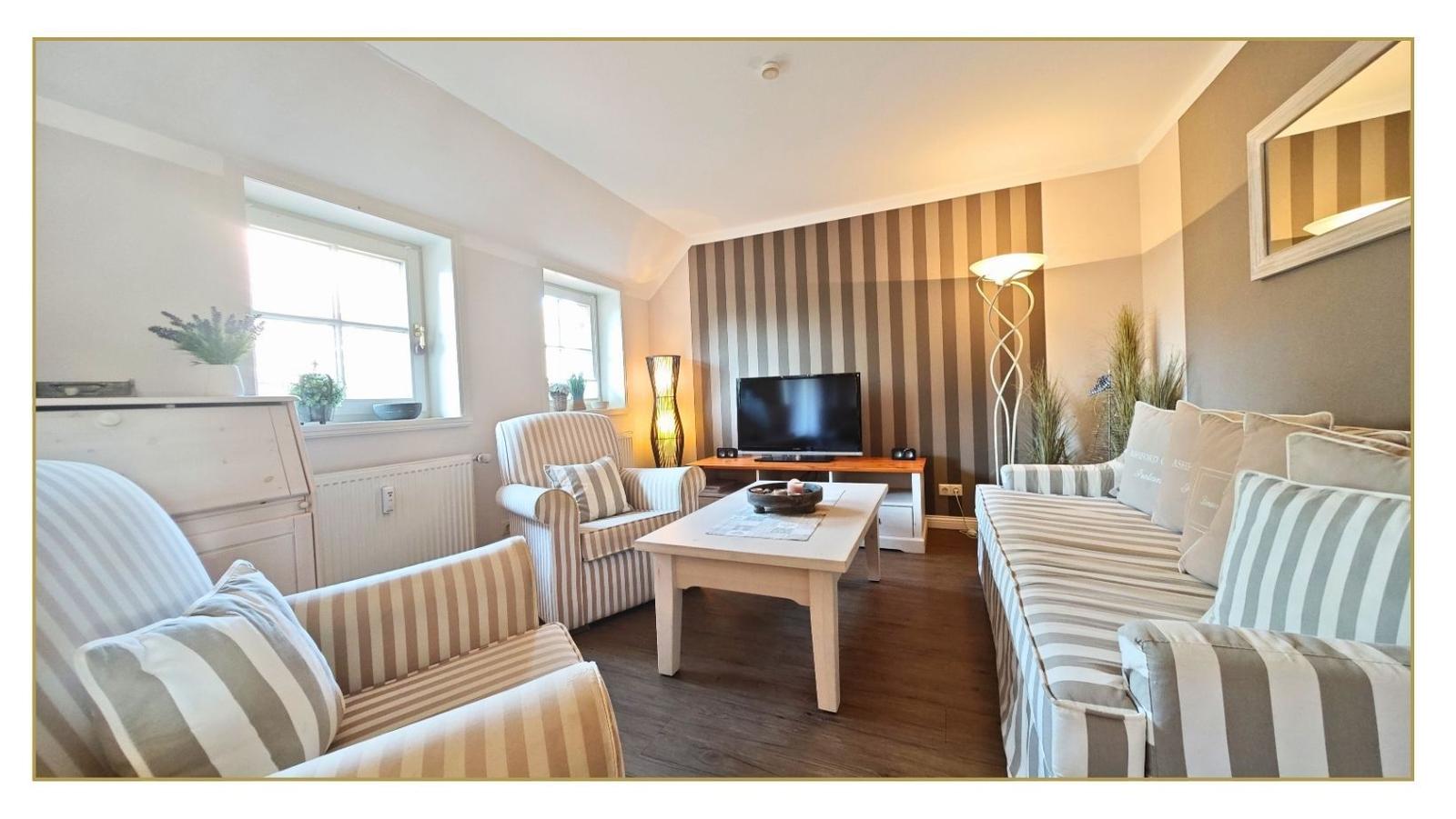 Wohnzimmer mit Sofa, Sessel, Tisch und Fernseher. Wand mit Streifenmuster.