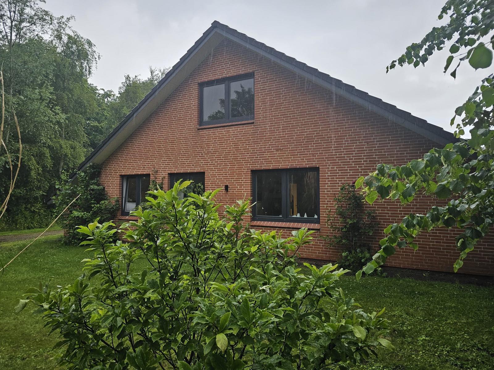 Rotes Backsteingebäude mit Fenstern und grünem Garten.