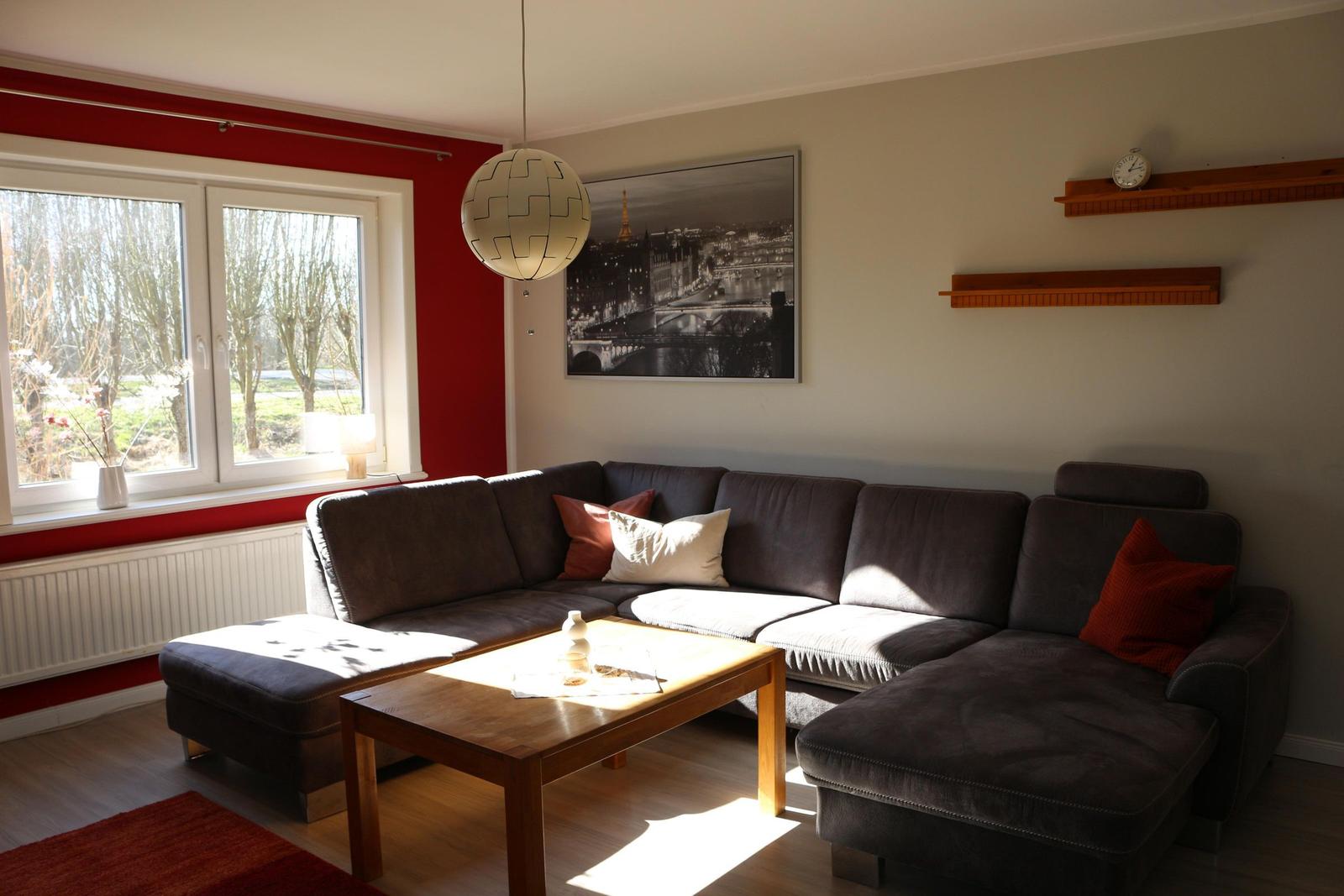 Wohnzimmer mit Ecksofa, Holztisch und Fenster mit Blick auf Grünfläche.