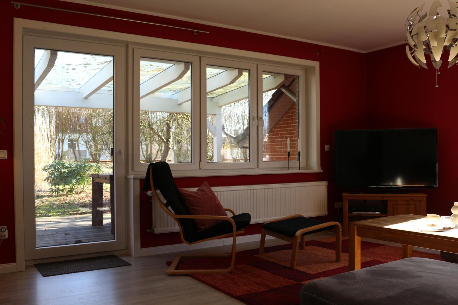 Wohnzimmer mit roten Wänden, Sitzgelegenheit und TV. Blick auf Terrasse und Garten.