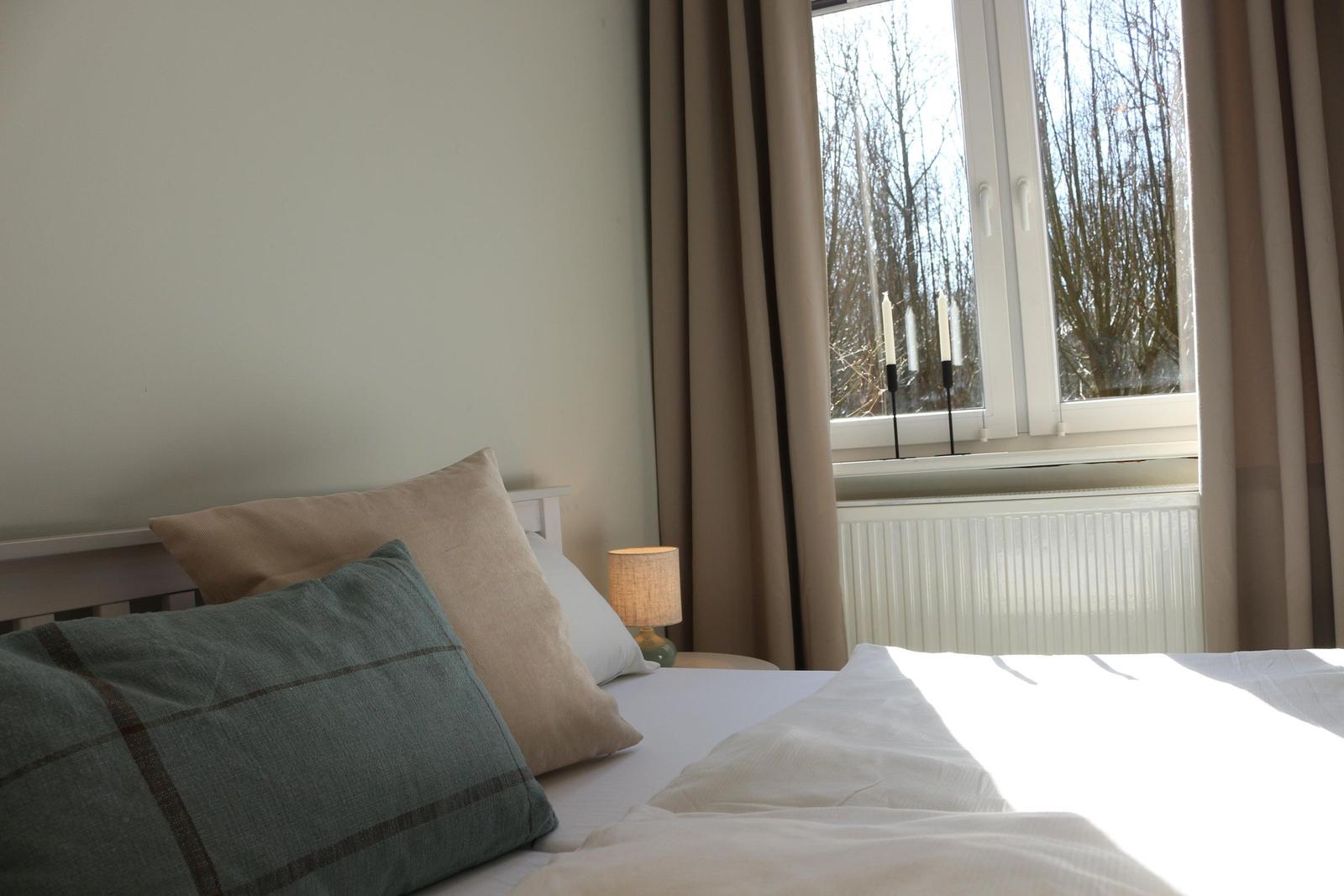 Ein Bett mit Kissen und einer Lampe neben einem Fenster mit Vorhängen.