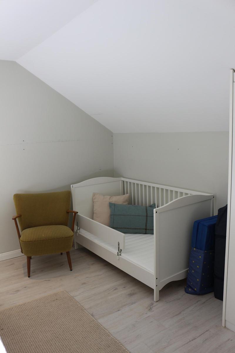 Kinderzimmer mit weißem Bett, gelber Sitzgelegenheit und Holzboden.