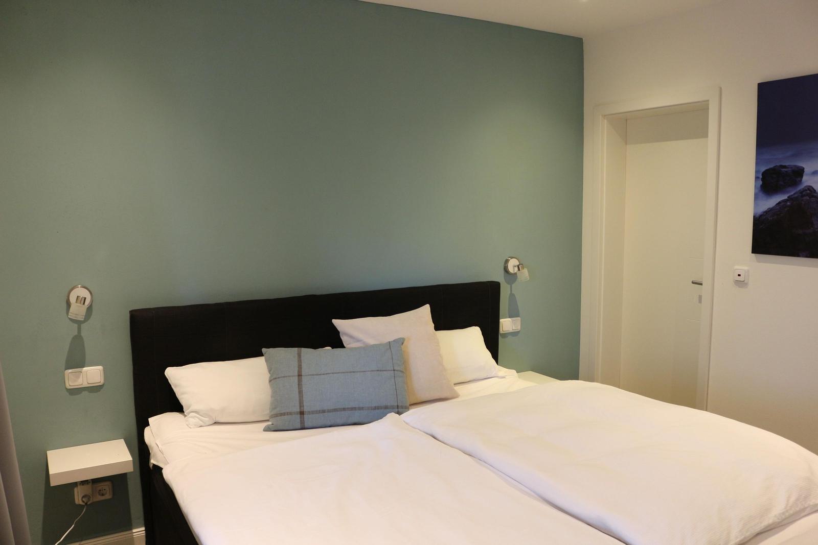Schlafzimmer mit Bett, Wandbeleuchtung und Wandbild.