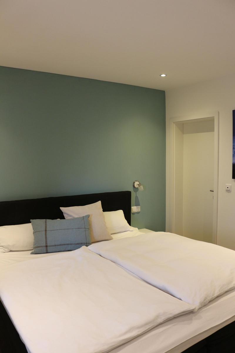 Schlafzimmer mit Doppelbett, grüner Wand und Nachttischbeleuchtung.