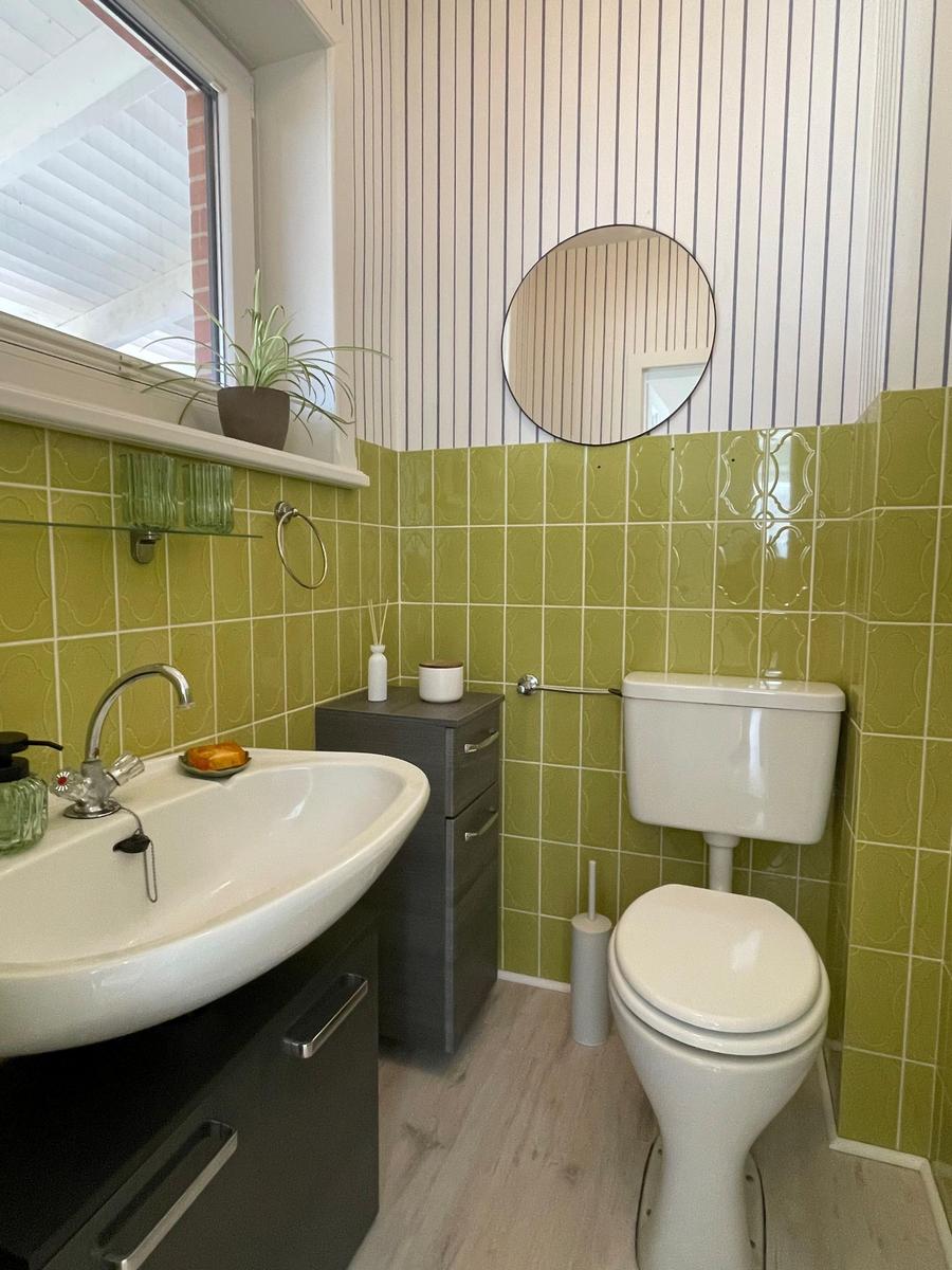 Badezimmer mit grünen Fliesen, Waschbecken, Toilette und Spiegel.