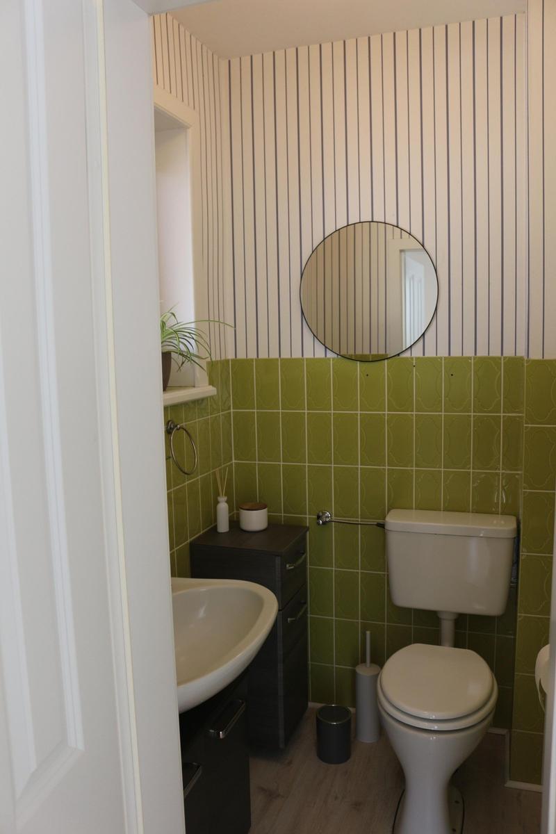 Badezimmer mit Toilette, Waschbecken und Spiegel an gestreifter Wand.