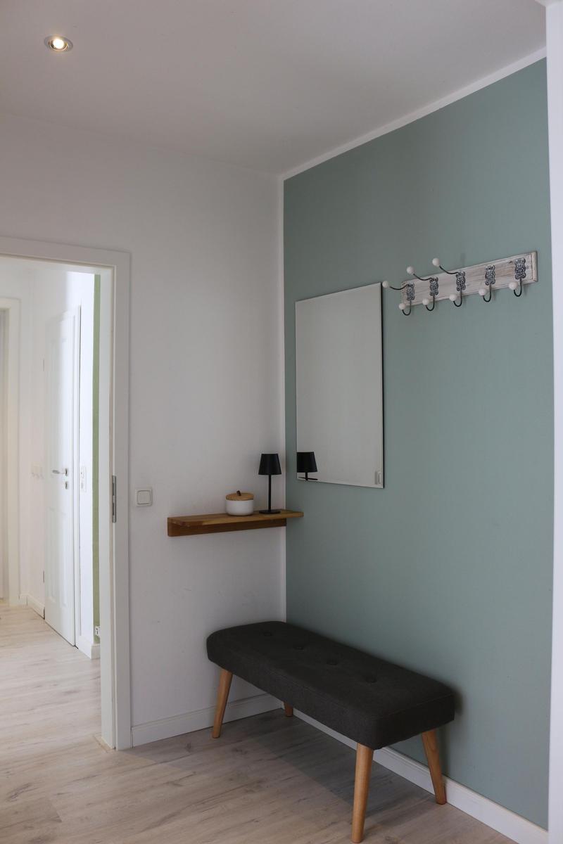 Eingangsbereich mit Bank, Wandgarderobe und Spiegel an mintfarbener Wand.