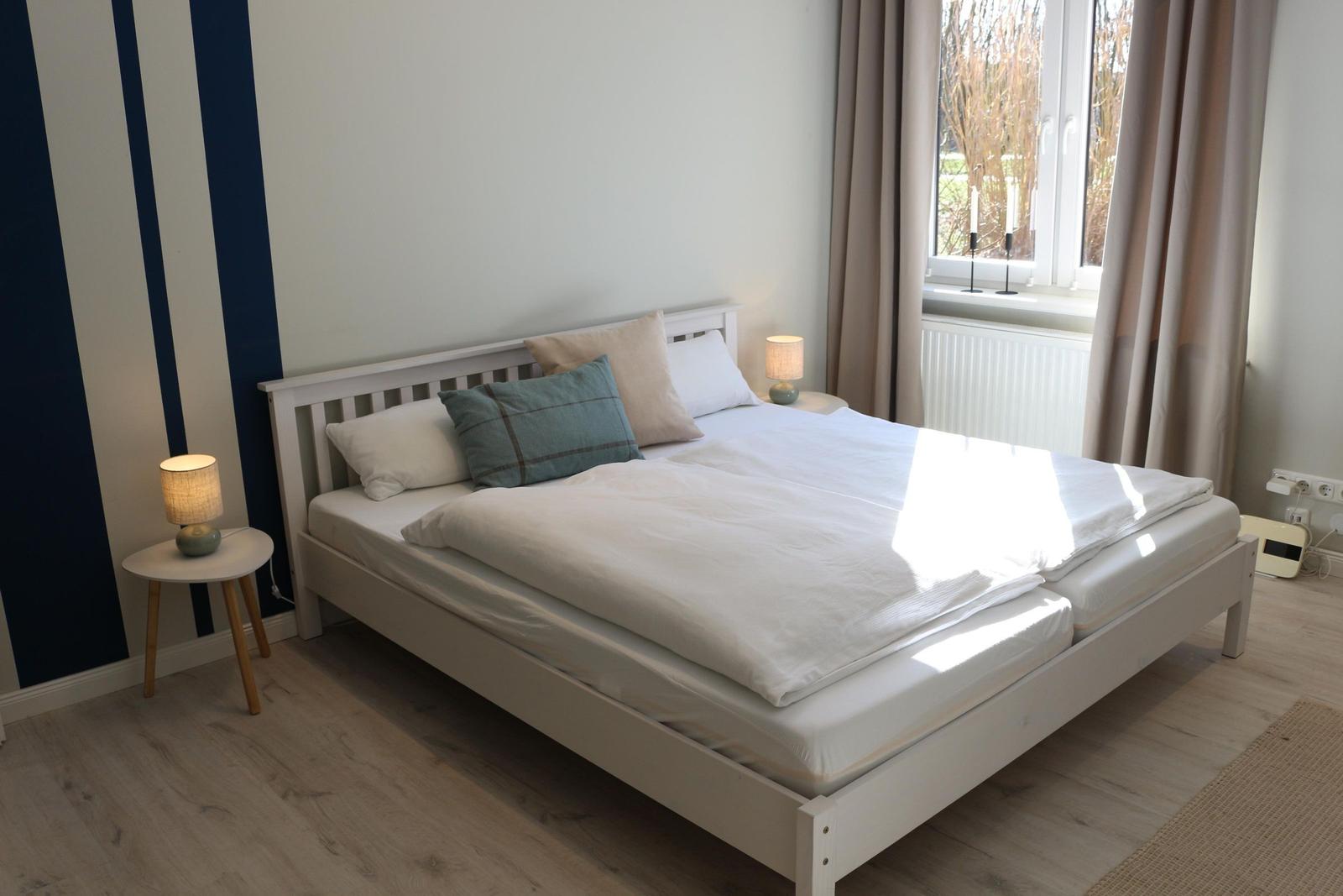 Schlafzimmer mit Doppelbett, zwei Nachttischen und Fenster mit Vorhängen.