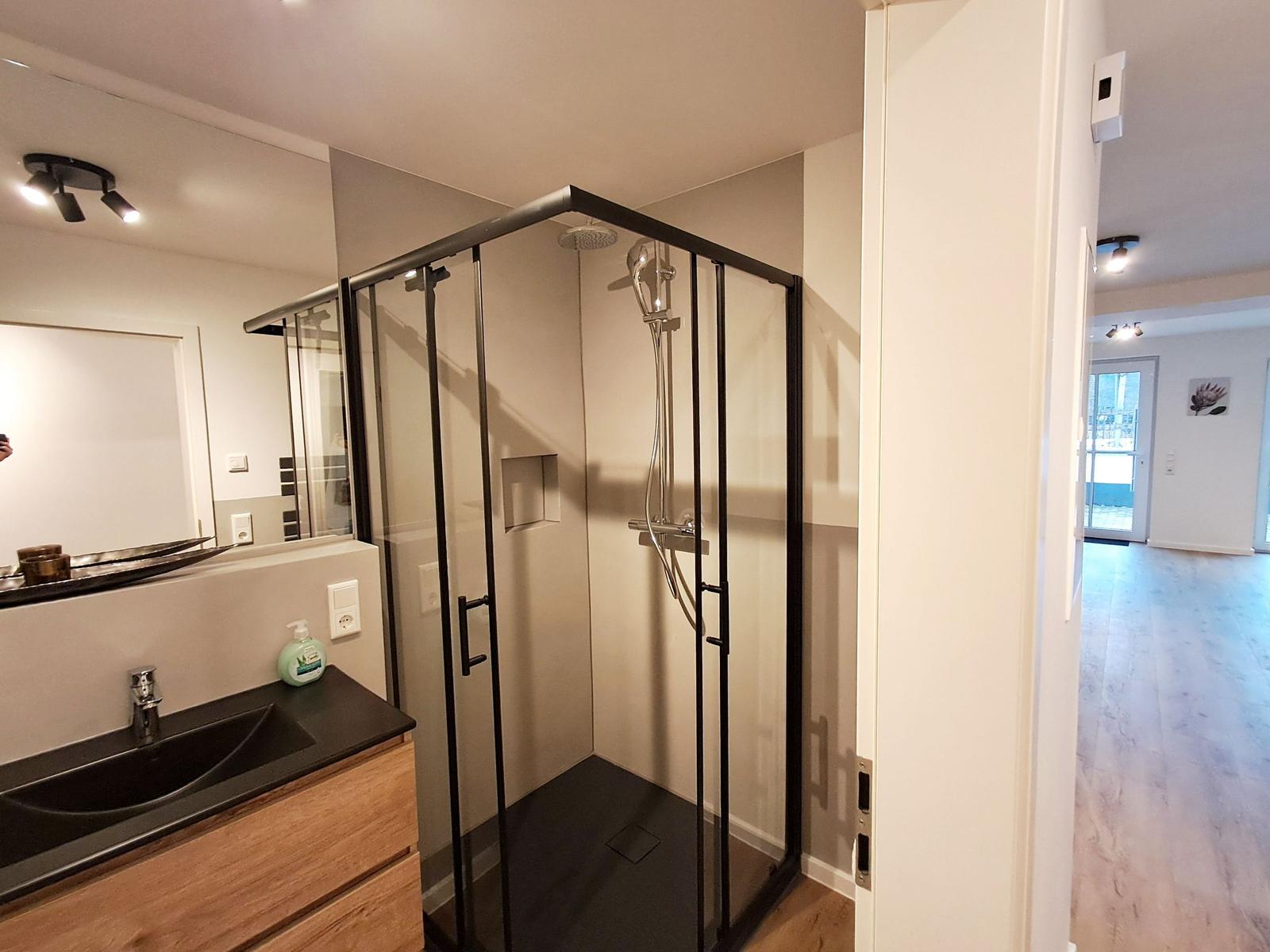 Dusche mit Glaswand, Waschbecken und Spiegel im Bad