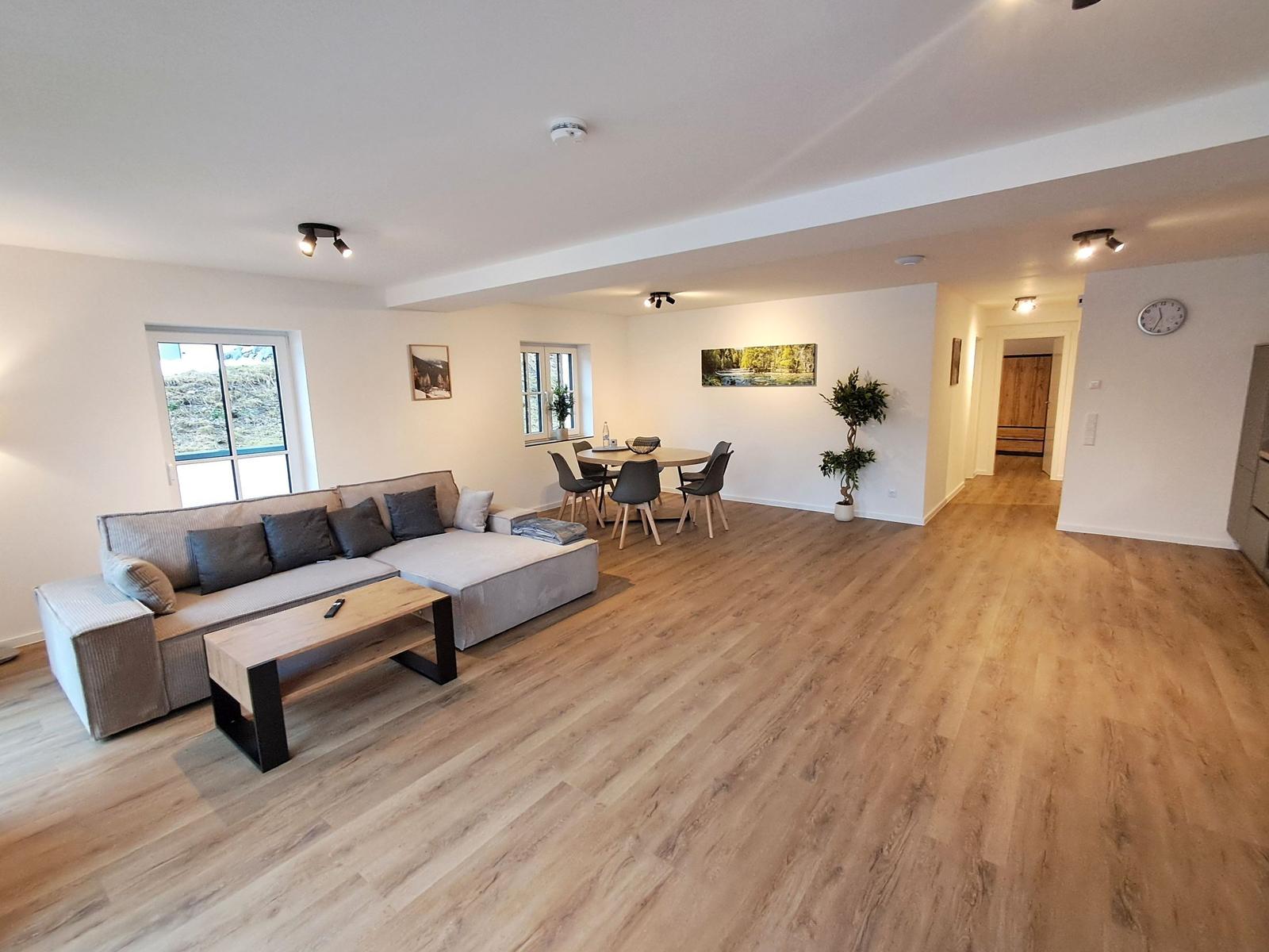 Wohn- und Essbereich mit Sofa, Tisch und Stühlen auf Holzboden.