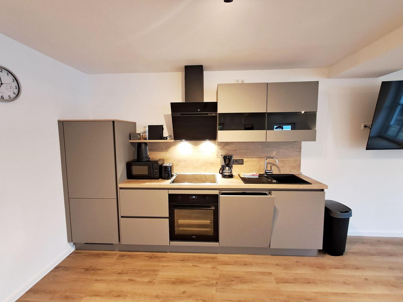 Küche mit Dunstabzug, Spüle und Backofen. Holzfußboden und Wanduhr sichtbar.