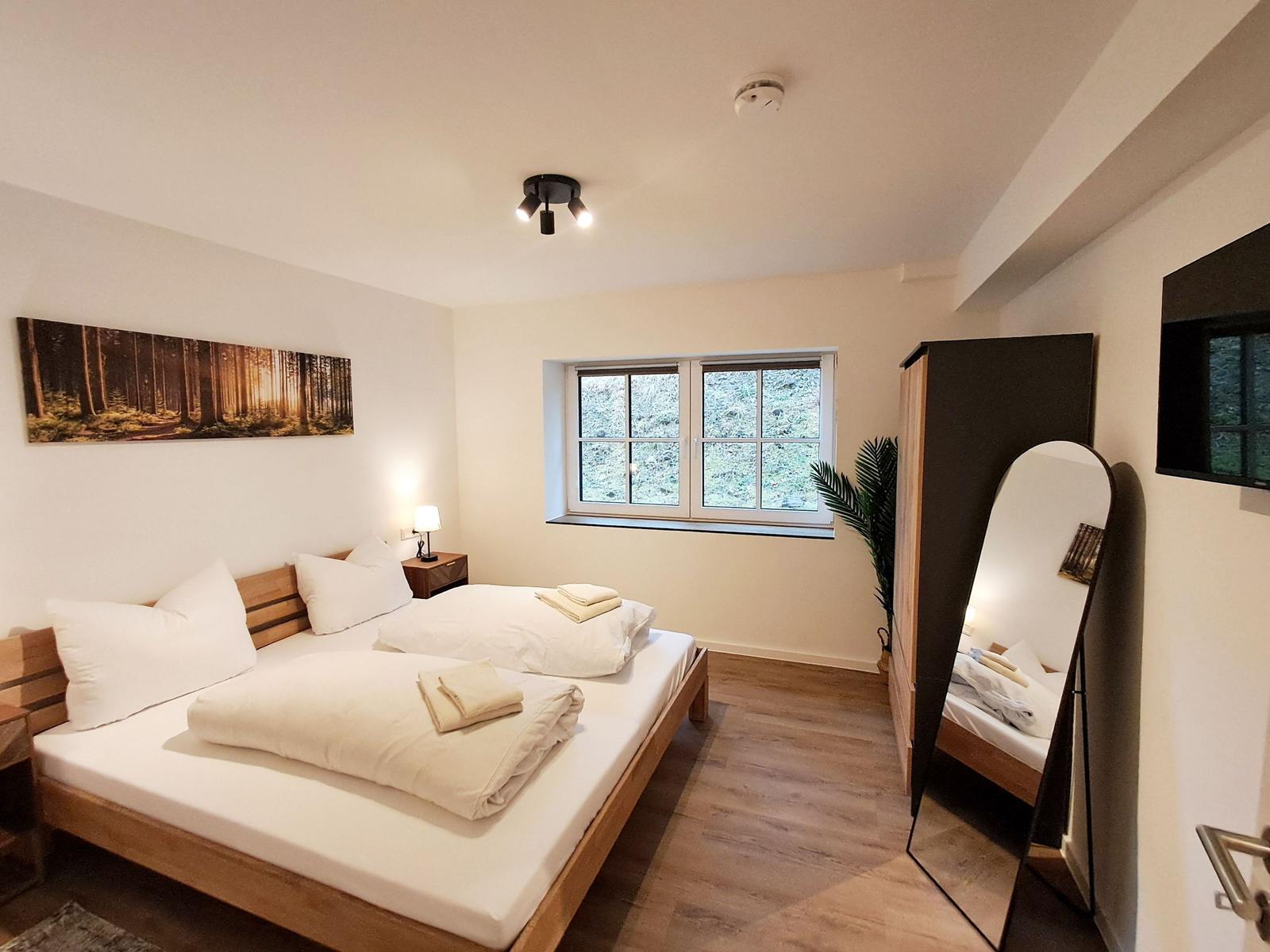 Schlafzimmer mit Bett, Fenster und Spiegel.