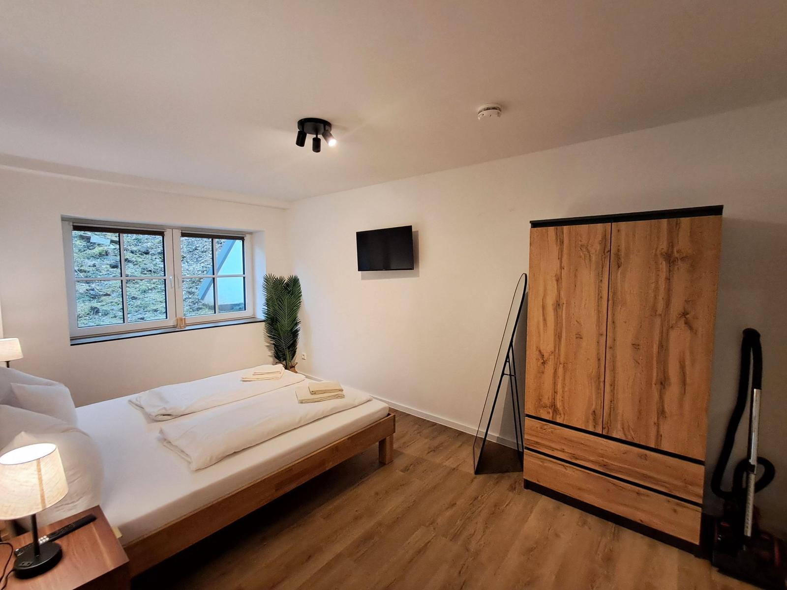 Schlafzimmer mit Bett, Kleiderschrank und Fernseher an der Wand.