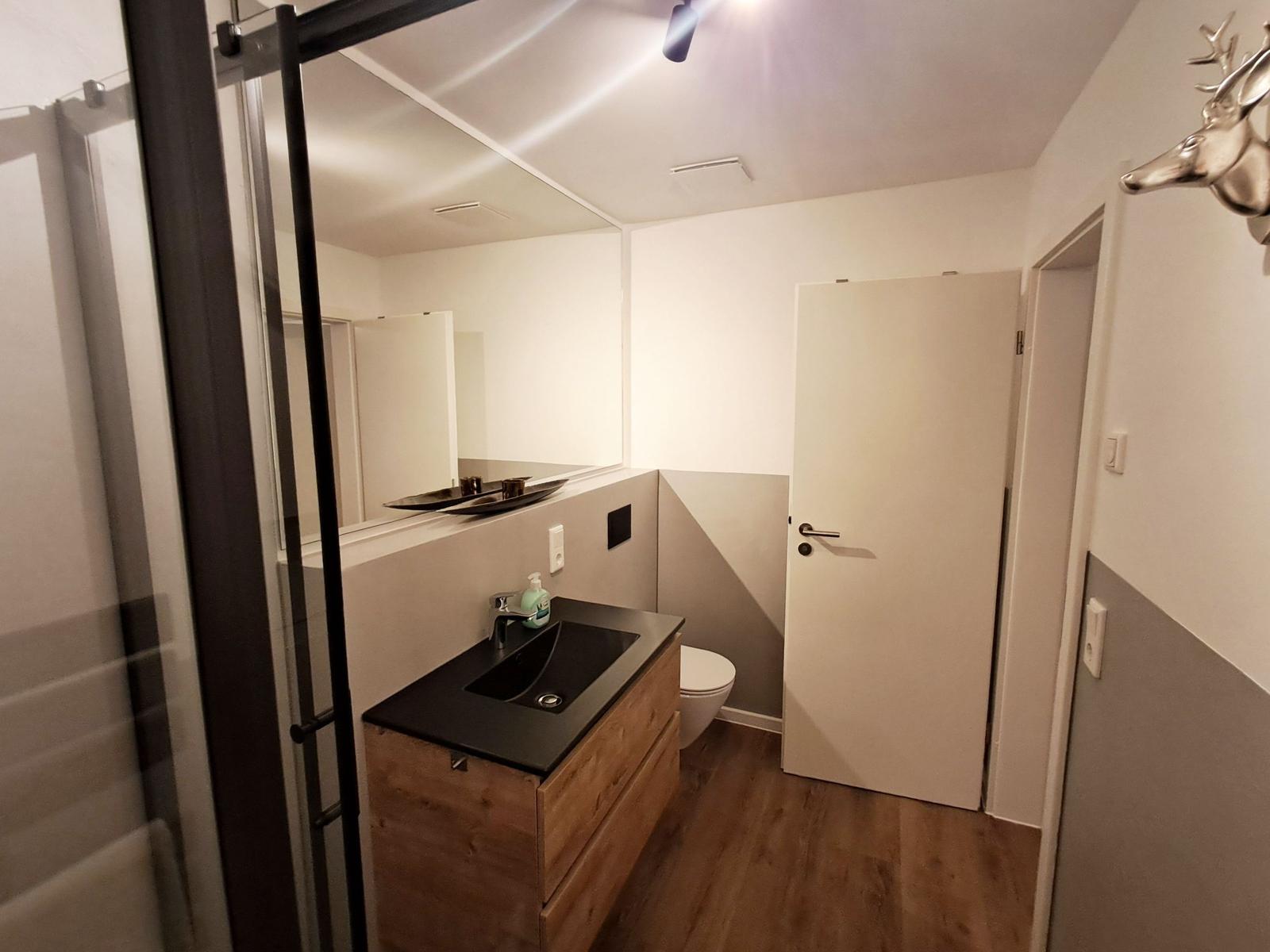 Badezimmer mit Dusche, Waschtisch und Toilette. Holzfußboden und Wanddekoration.