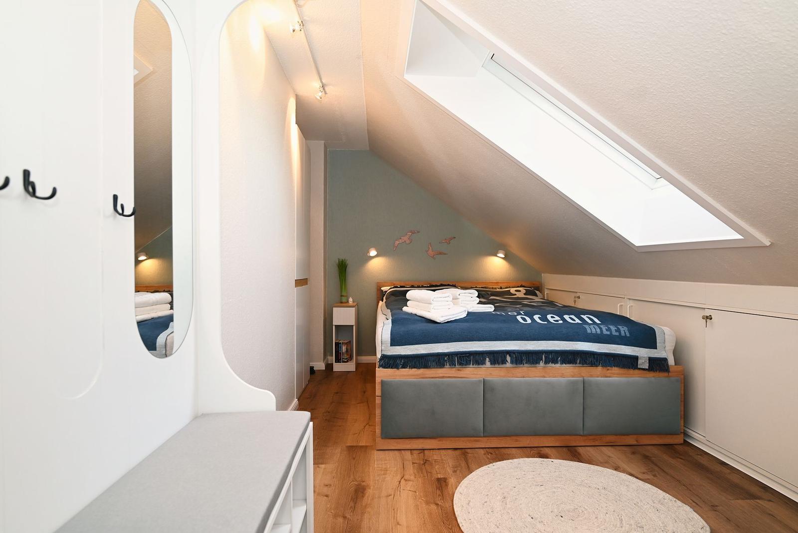 Schlafzimmer mit Dachschräge, Bett, Kleiderschrank und Dachfenster.