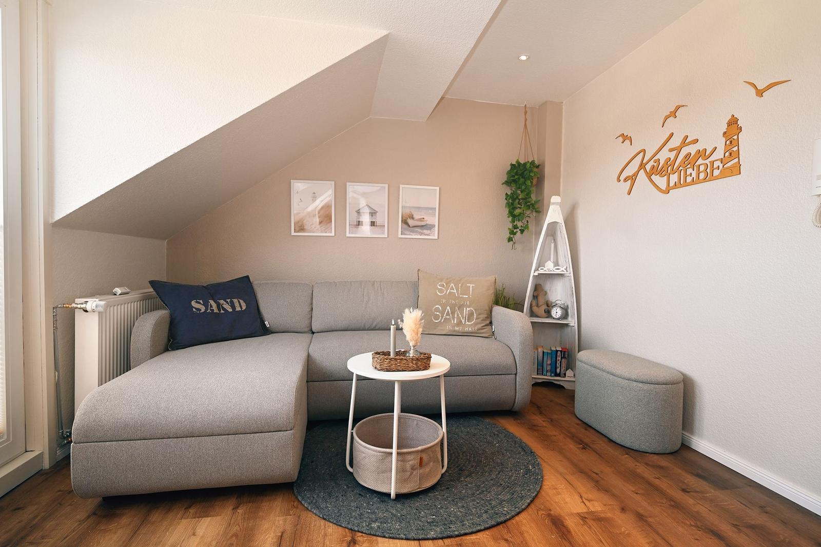 Wohnzimmer mit grauem Sofa, runden Tisch und Holzboden unter schrägen Dach