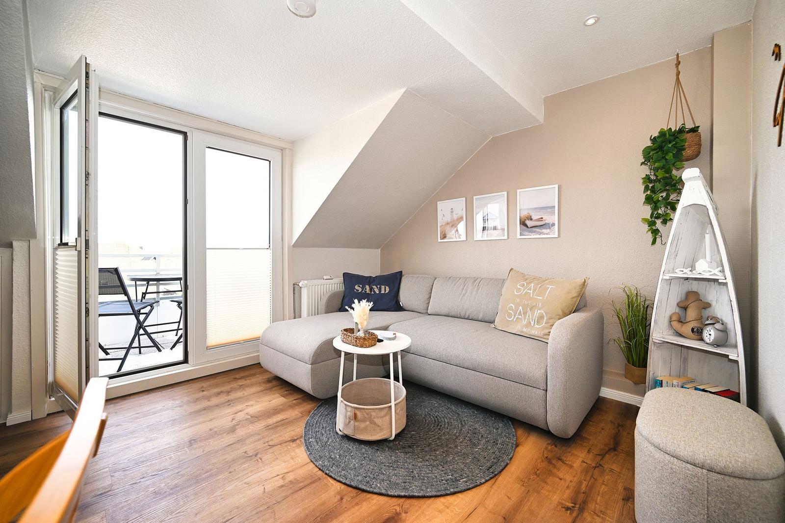 Wohnzimmer mit Sofa, Balkon und Wandregal. Holzboden und Dachschräge.