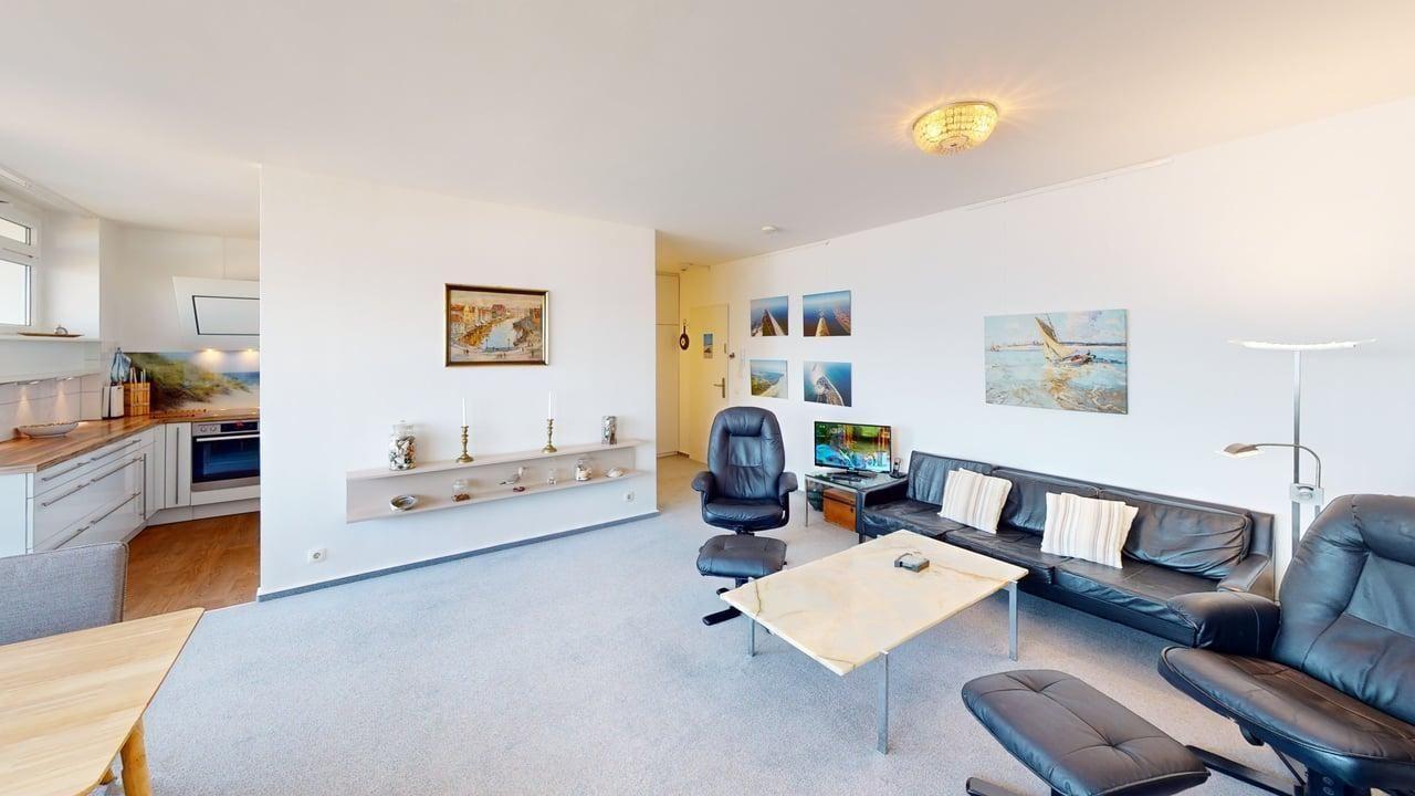 Wohnbereich mit Sofa, Sessel und Küchenbereich. Wandbilder und Beleuchtung.