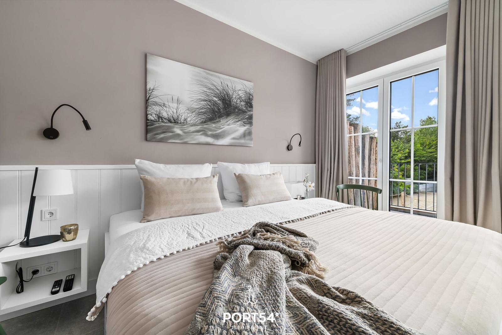 Schlafzimmer mit Bett, Wandbild und Fenster zum Balkon.