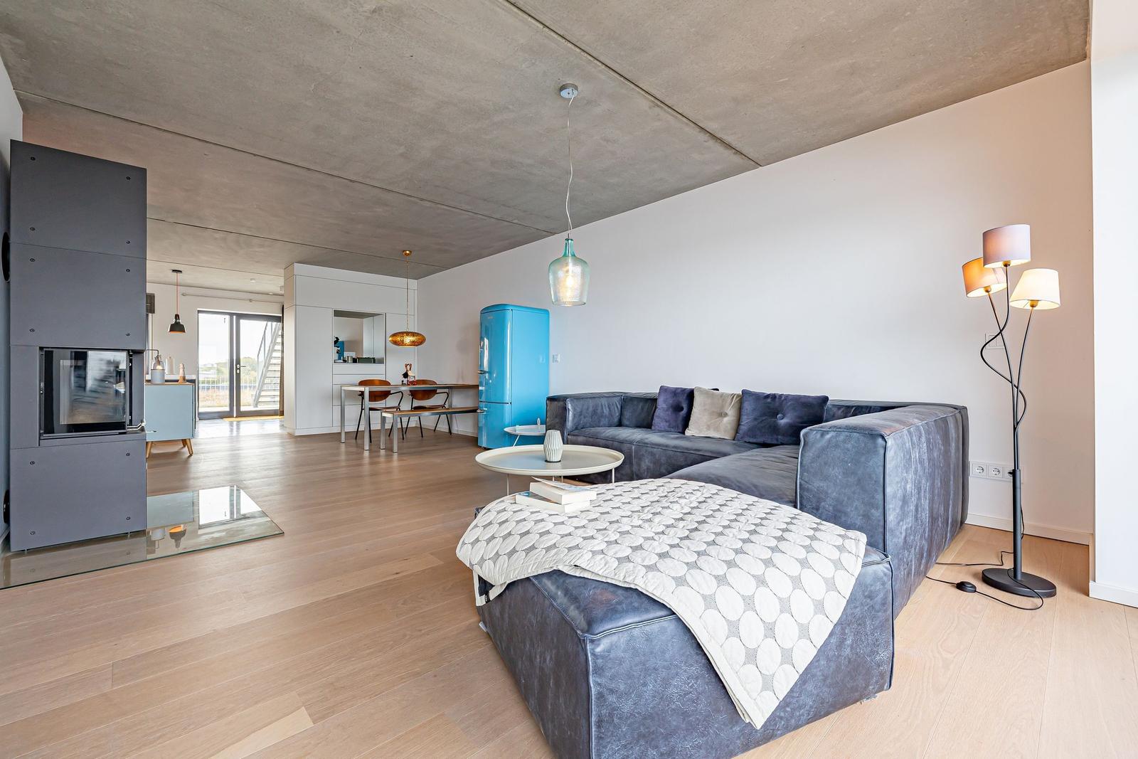 Wohnzimmer mit Sofa, Couchtisch und blauem Kühlschrank. Holzboden und Betondecke.