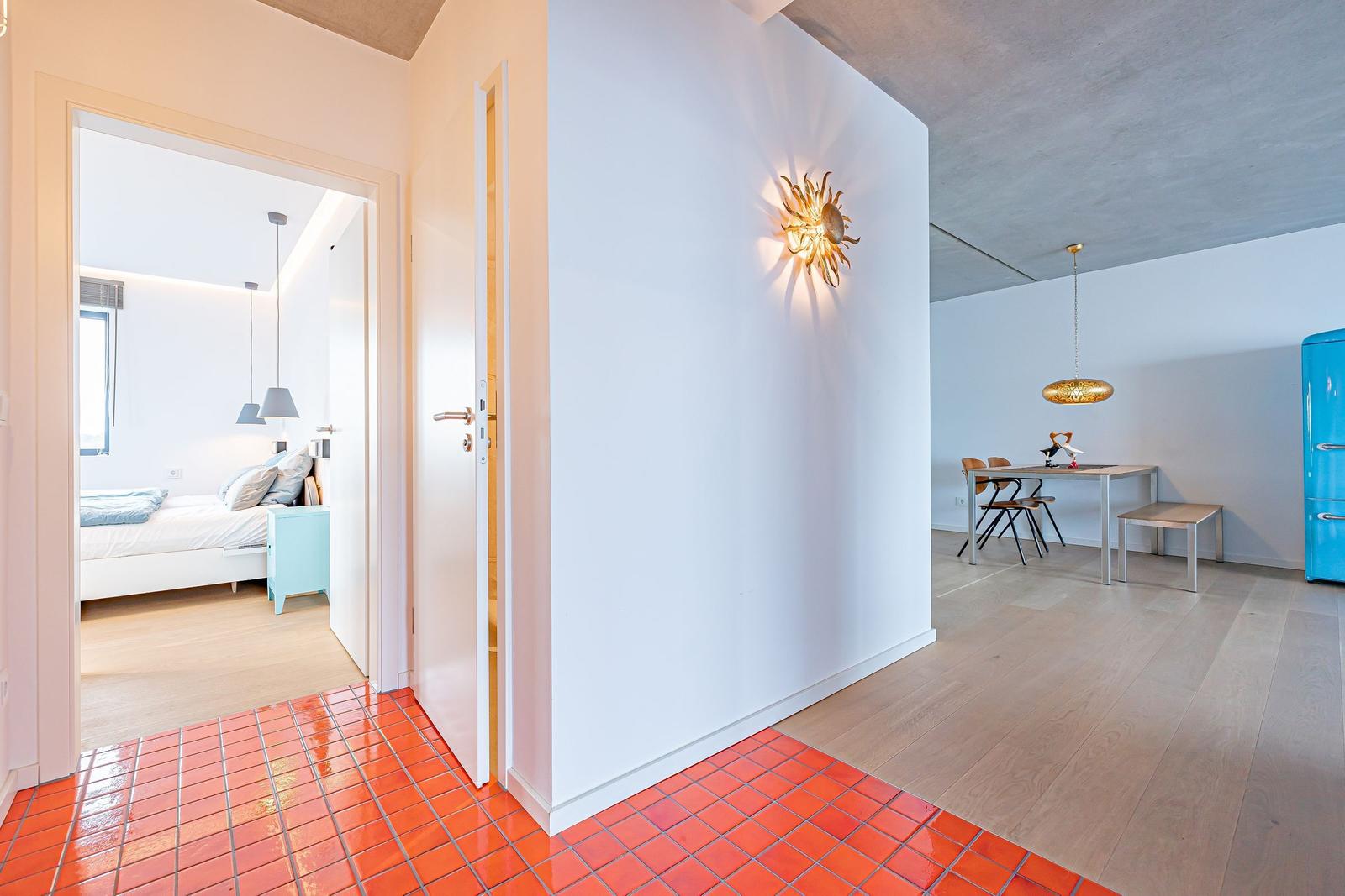 Eingangsbereich mit rotem Fliesenboden, Schlafzimmer und Essbereich mit blauem Kühlschrank.