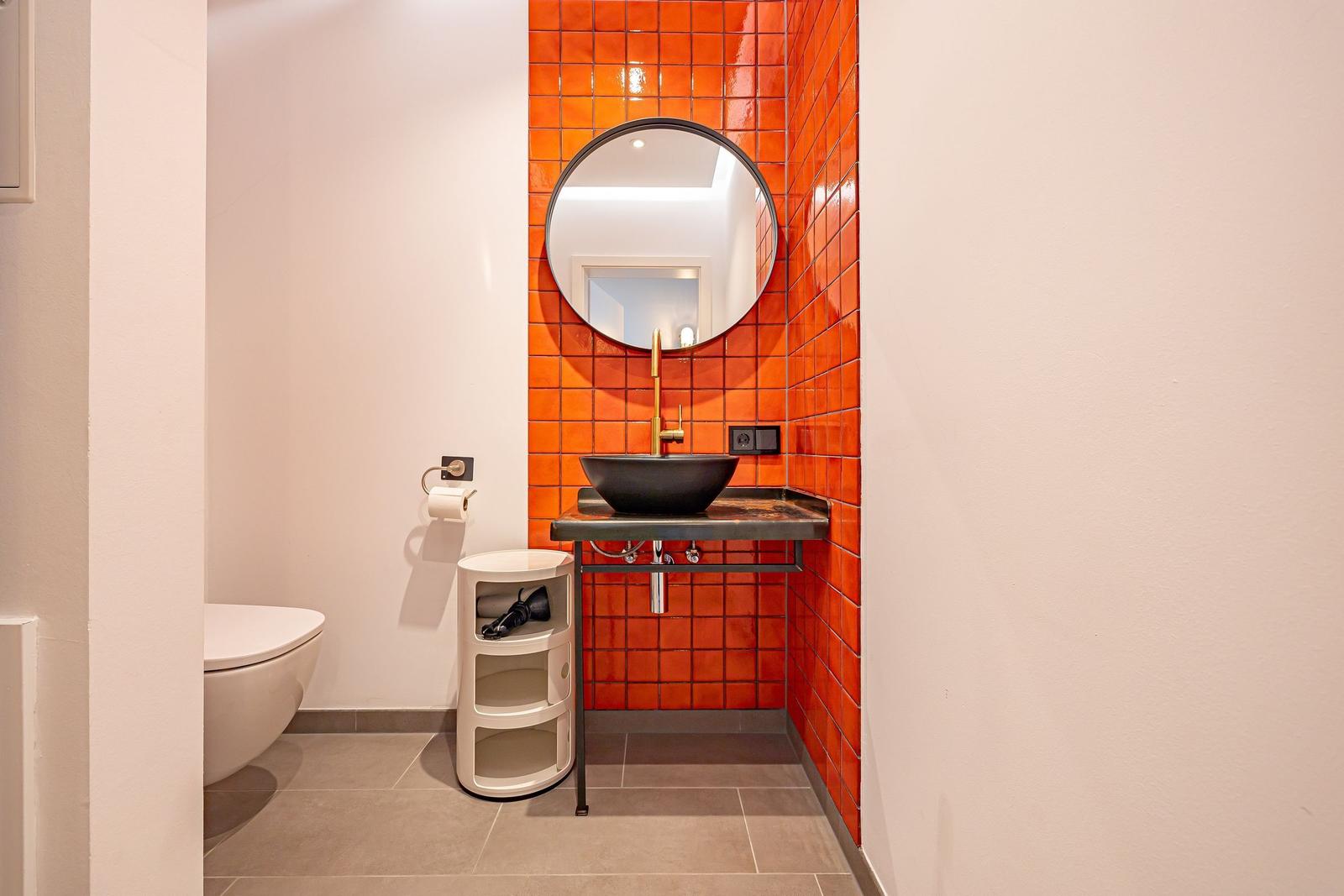Badezimmer mit orangefarbenen Fliesen, runden Spiegel und schwarzem Waschbecken.