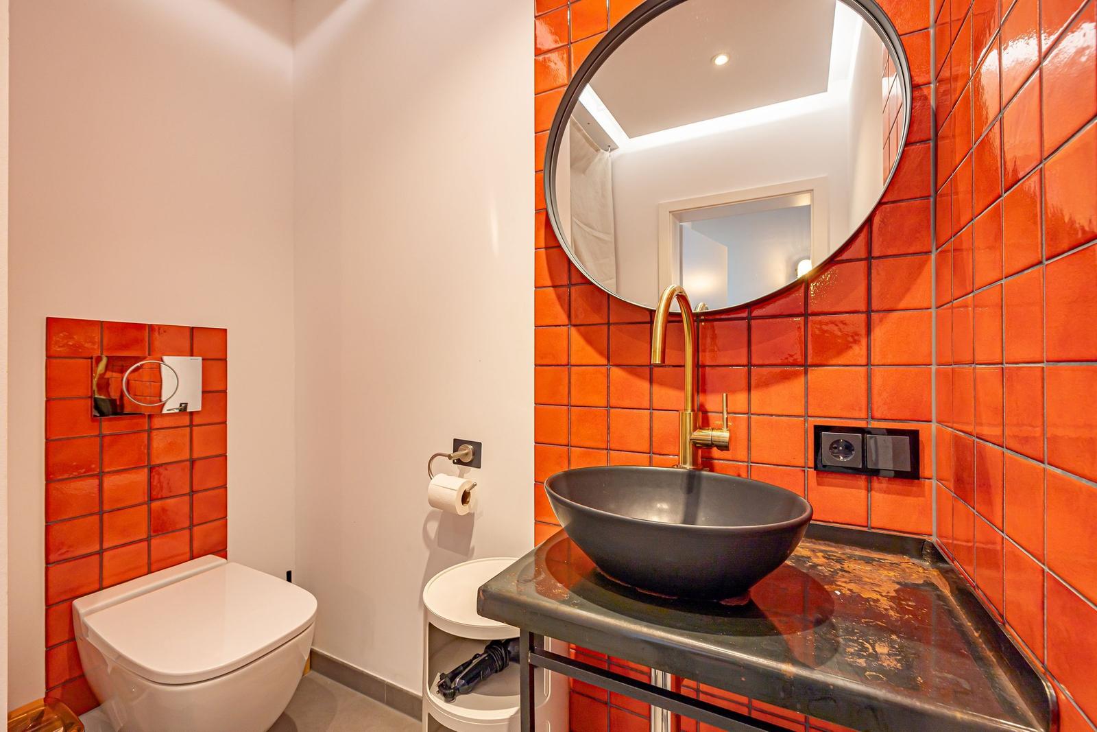 Badezimmer mit orangefarbenen Fliesen, runden Spiegel und schwarzer Waschschale.