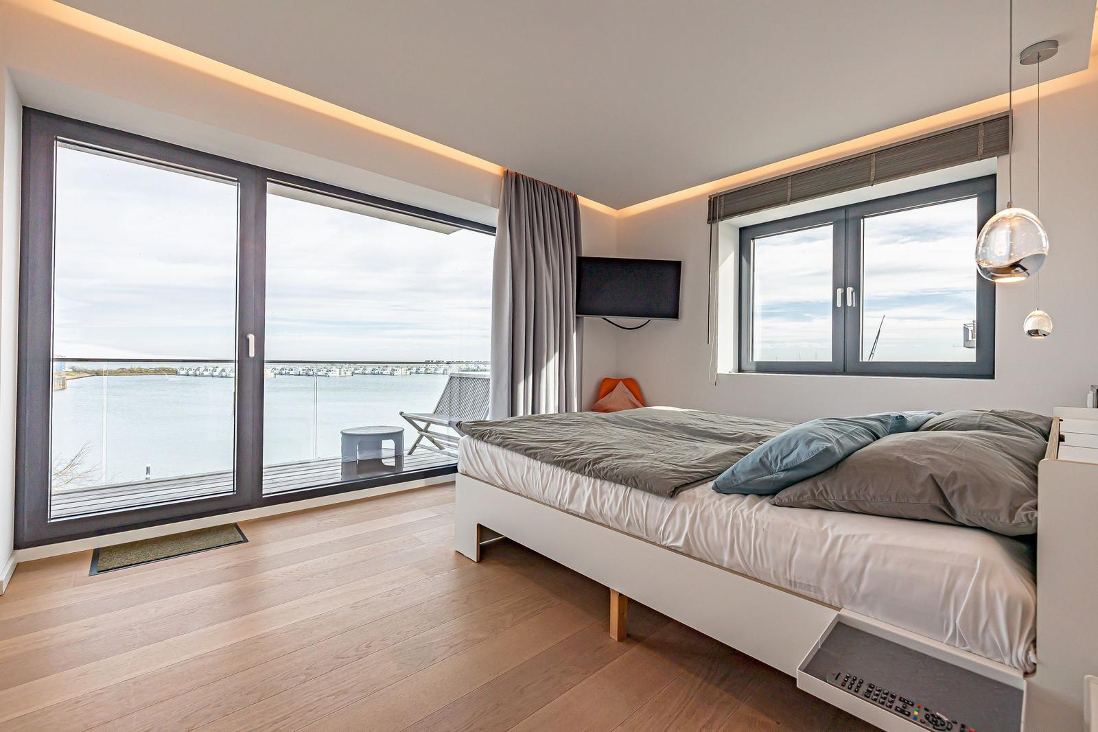 Schlafzimmer mit Blick auf Wasser, Bett, TV und Balkon.