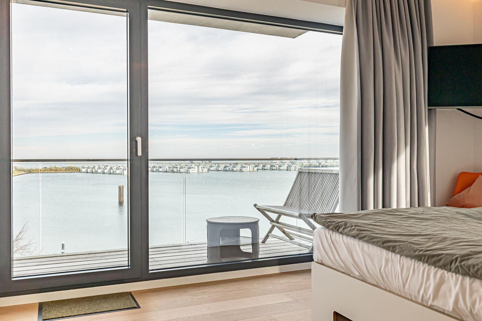 Zimmer mit Balkon und Blick auf Wasser und Häuser.