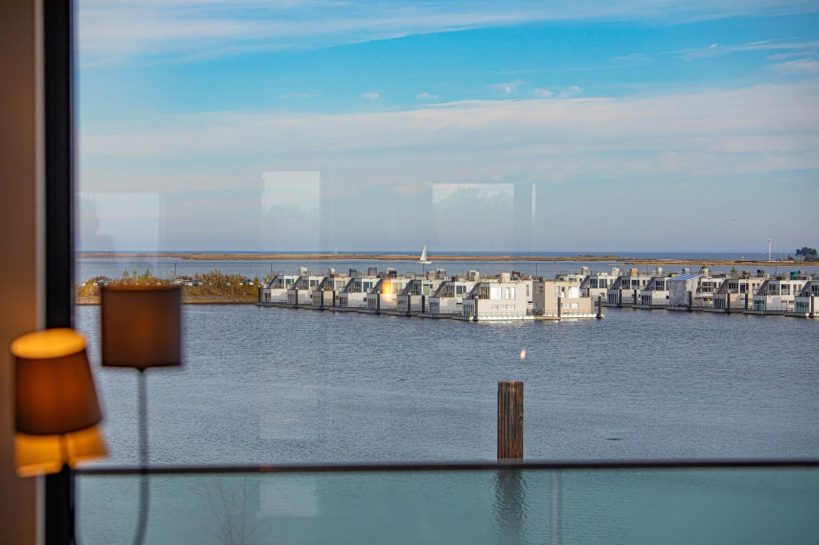 Blick auf Wasser und schwimmende Häuser mit Segelboot im Hintergrund.