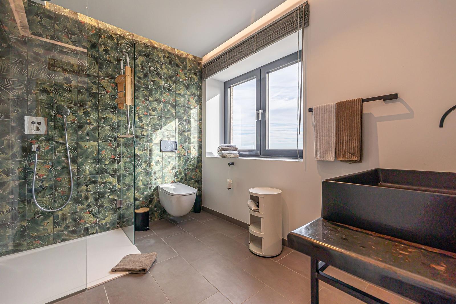 Badezimmer mit Dusche, Toilette und Waschbecken. Fenster mit Blick auf Meer.