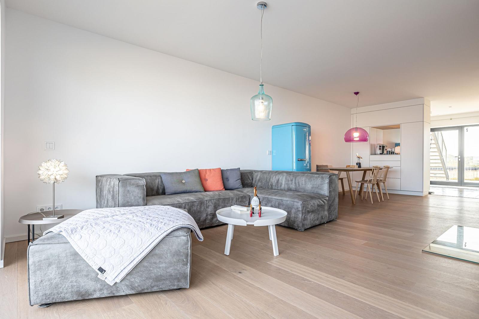 Wohnbereich mit grauem Sofa, blauem Kühlschrank und Holzboden.