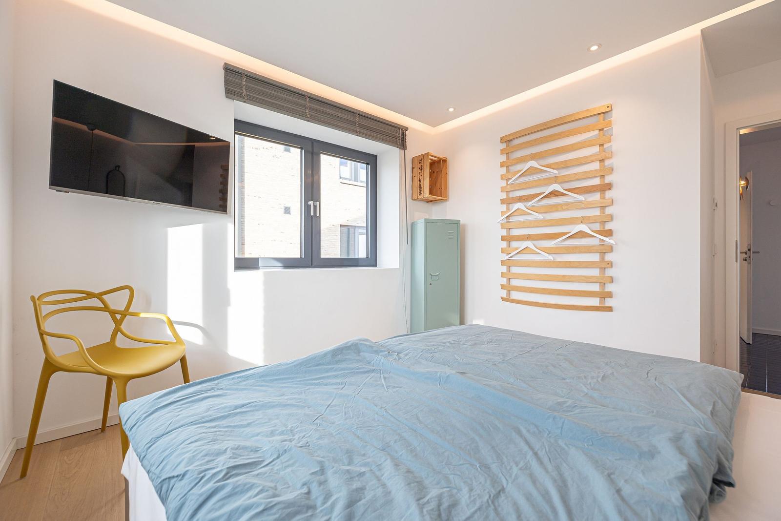 Schlafzimmer mit Bett, Fenster, TV und Kleiderständer.