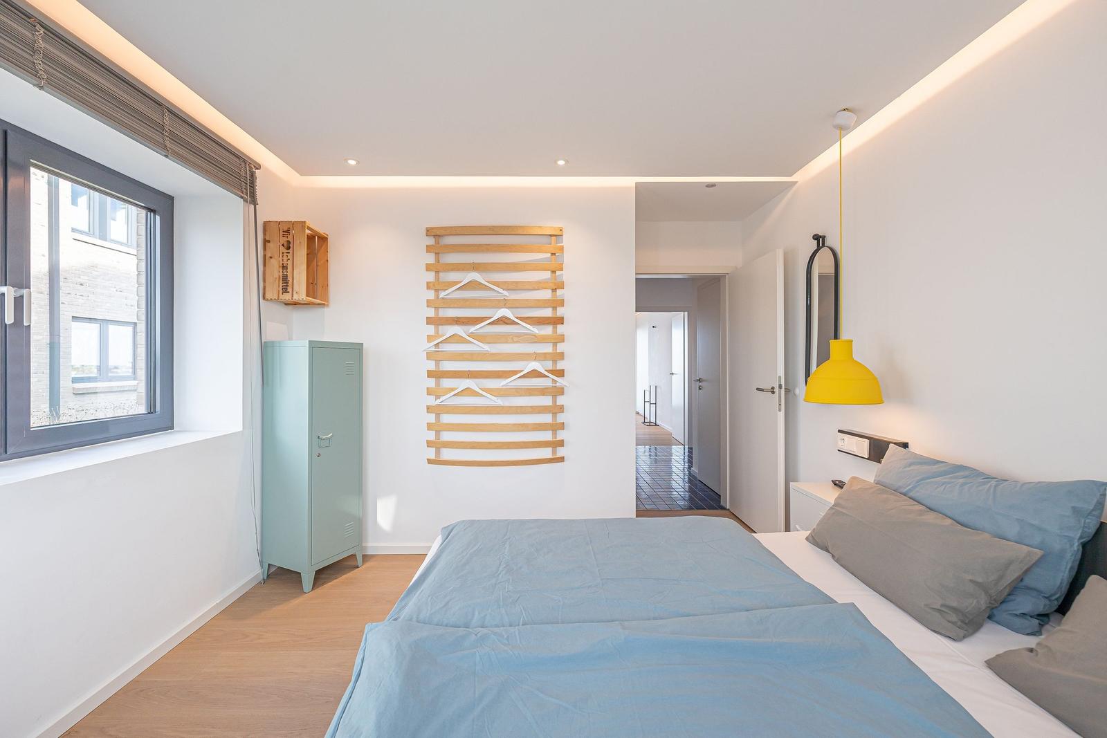 Schlafzimmer mit Bett, Kleiderschrank und Fenster. Wandregal mit Haken.