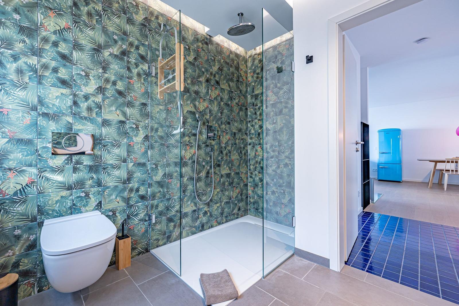 Bad mit Dusche und tropischen Fliesen. Durchgang zu Küche mit blauem Kühlschrank.