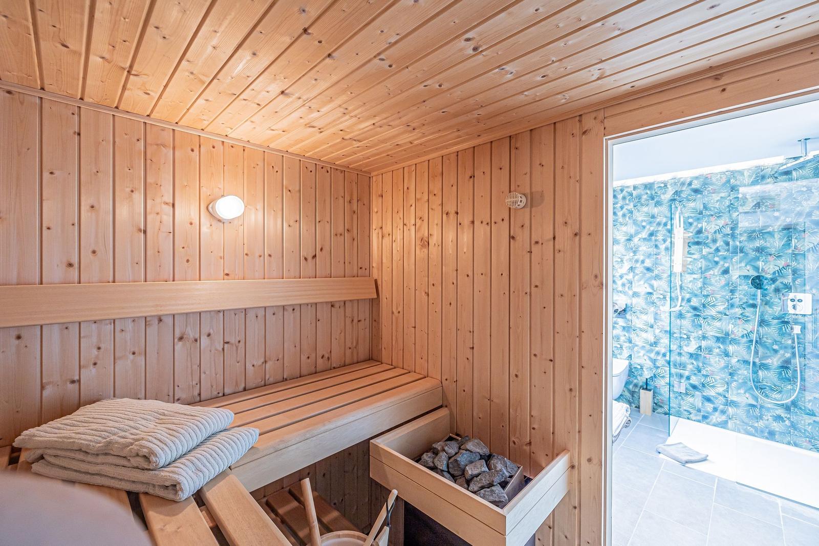 Sauna mit Holzwand und Bank. Durchgang zu Dusche mit blauem Mosaik.