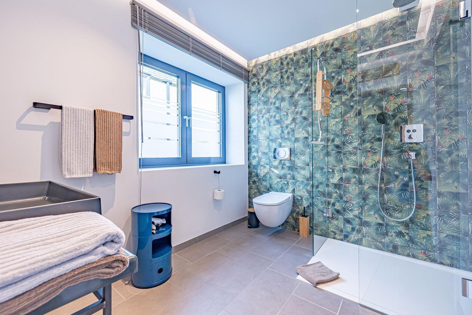 Bad mit Dusche, Toilette und Waschtisch. Wandfliesen mit tropischem Motiv.