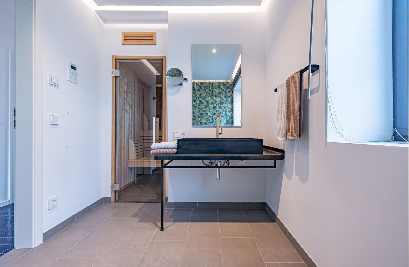 Badezimmer mit Waschtisch, Spiegel und Sauna im Hintergrund.