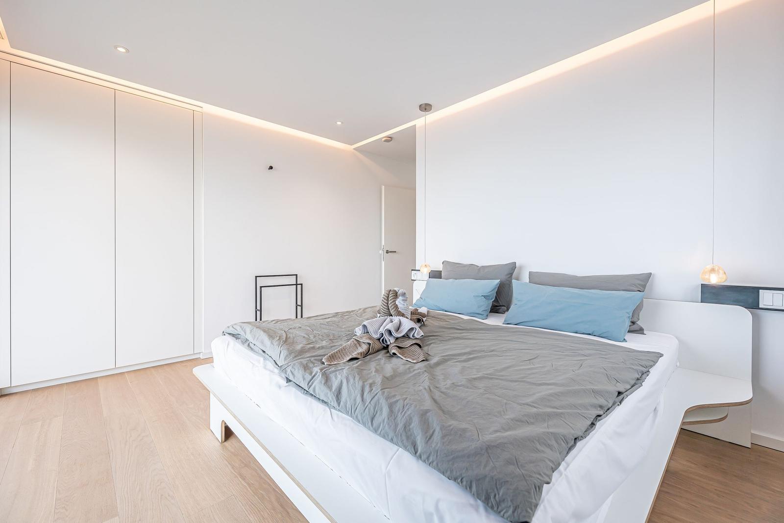 Schlafzimmer mit weißem Bett, grauer Bettwäsche und integriertem Schrank.