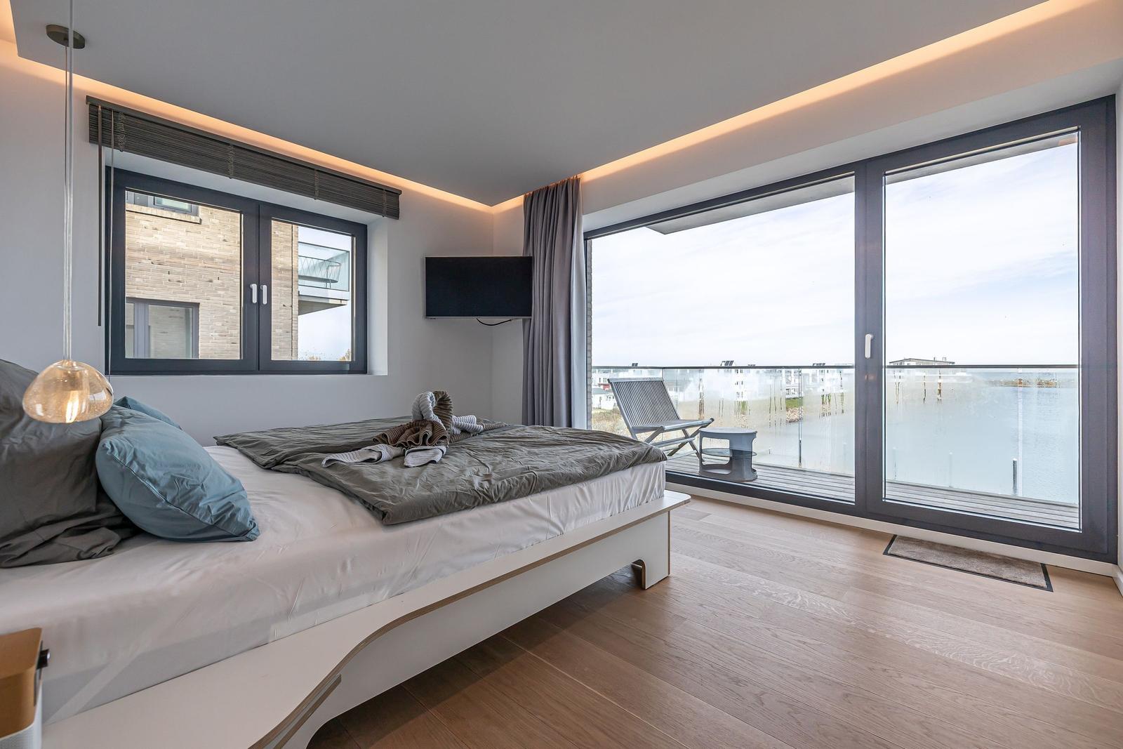 Schlafzimmer mit Balkon, großes Bett und TV. Blick auf Wasser.