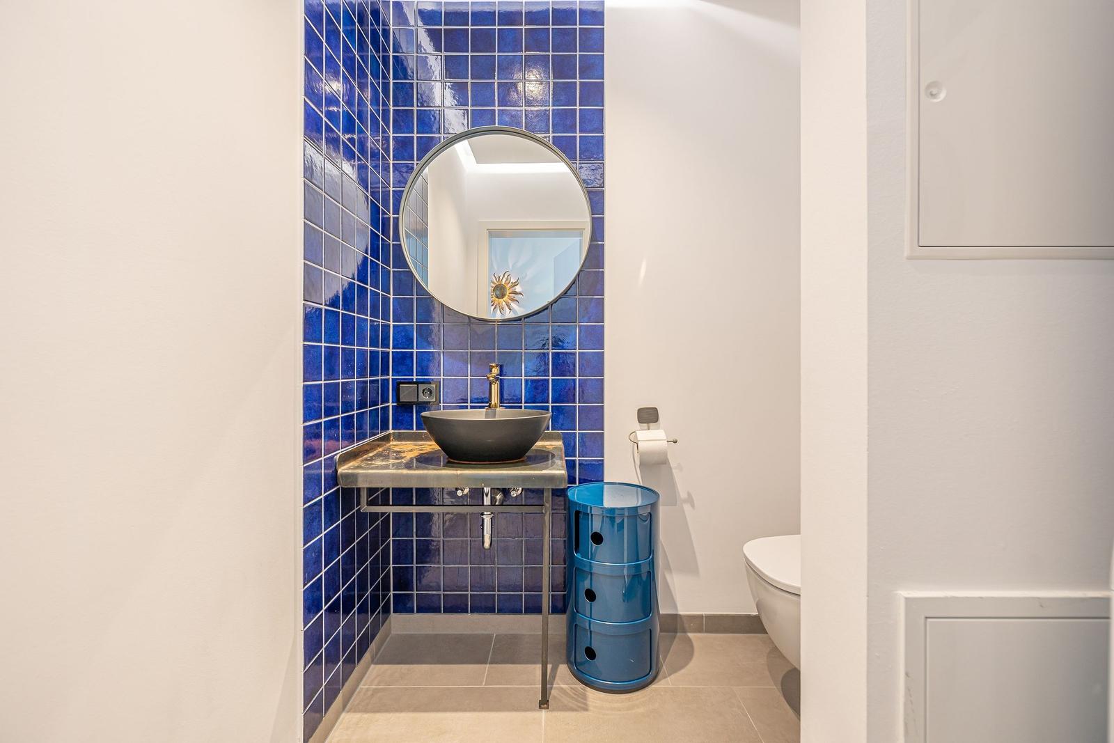 Badezimmer mit blauen Fliesen, runden Spiegel und Waschtisch