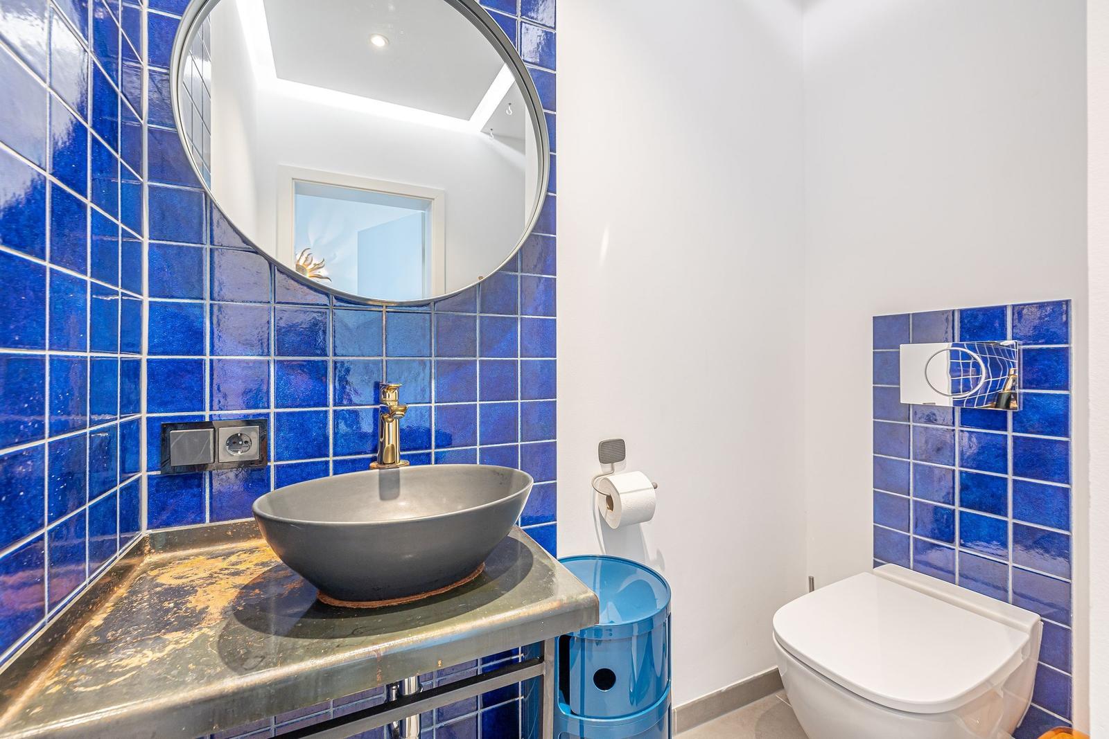 Badezimmer mit blauen Fliesen, runden Spiegel und Waschbecken auf Metallplatte.