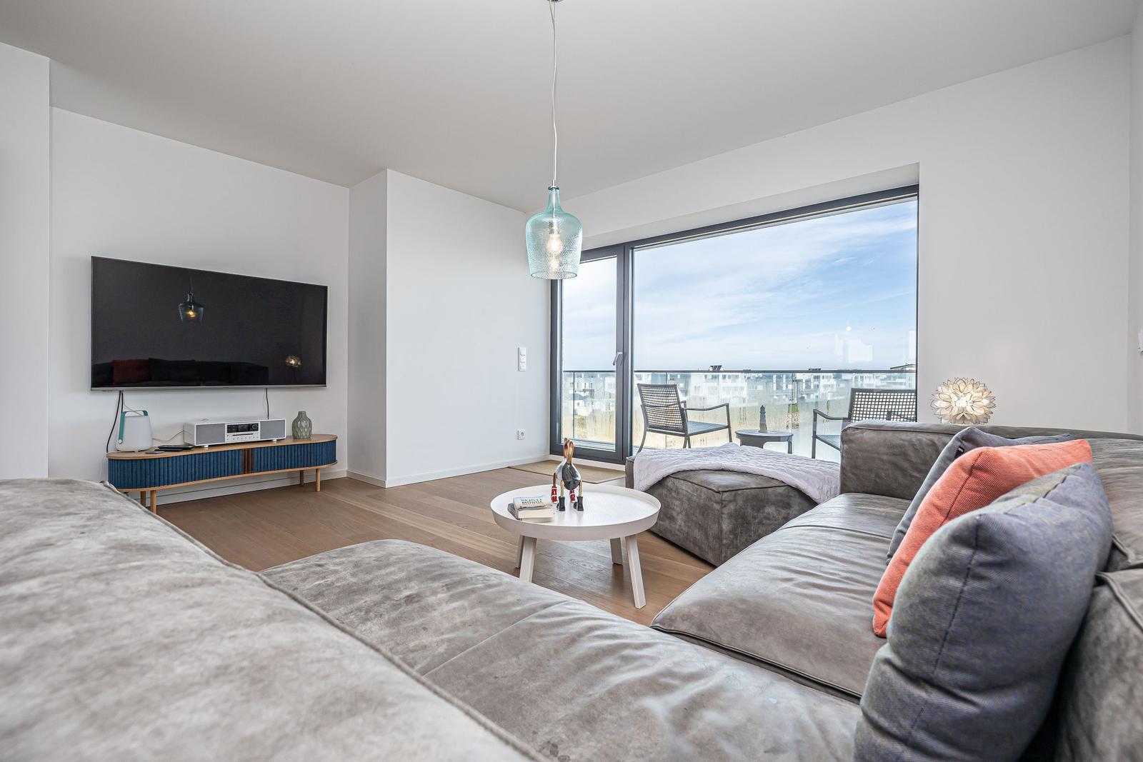 Wohnzimmer mit Sofa, Fernseher und Balkonansicht