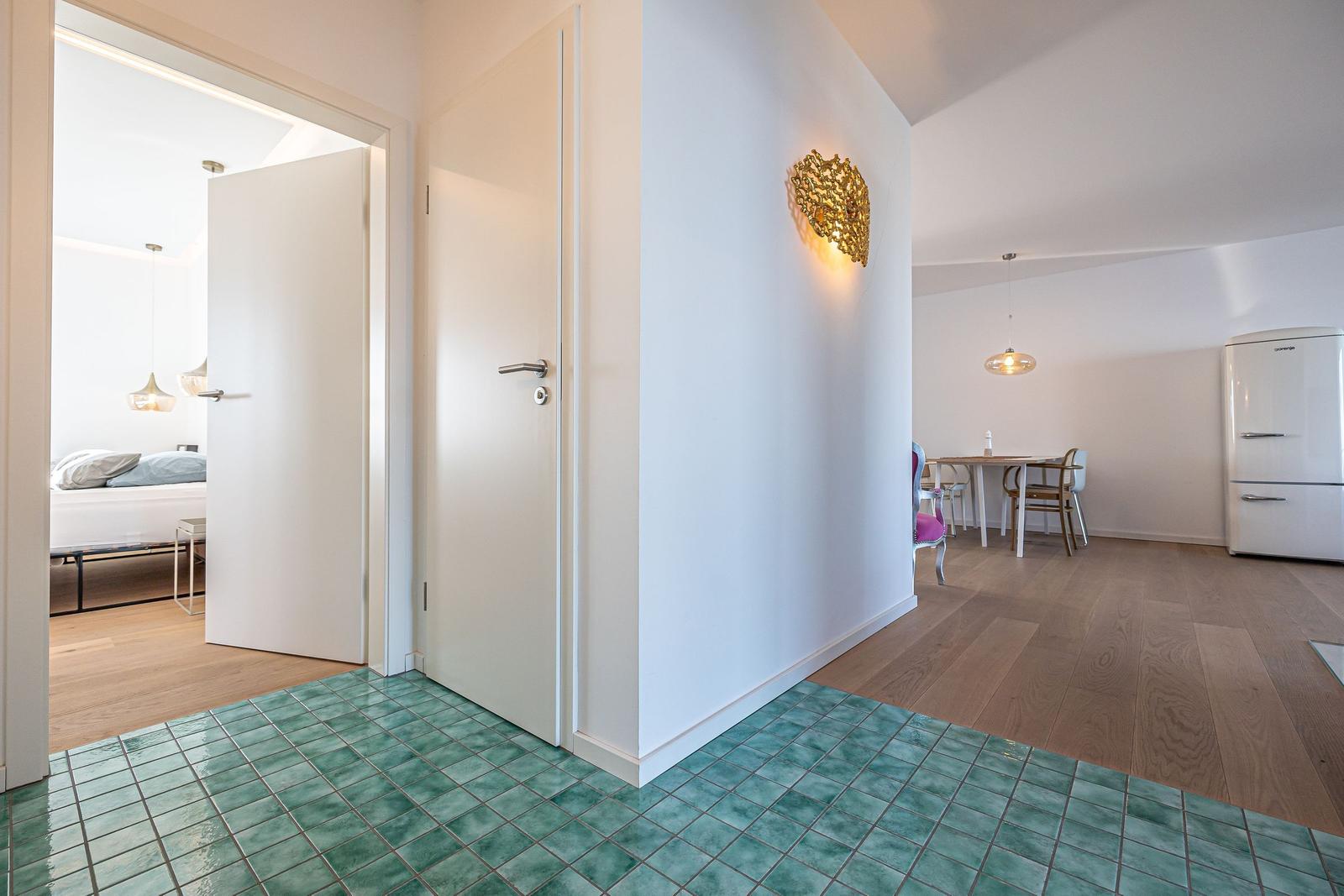 Flur mit grünem Fliesenboden, Tür zu Schlafzimmer und Essbereich mit Kühlgerät.