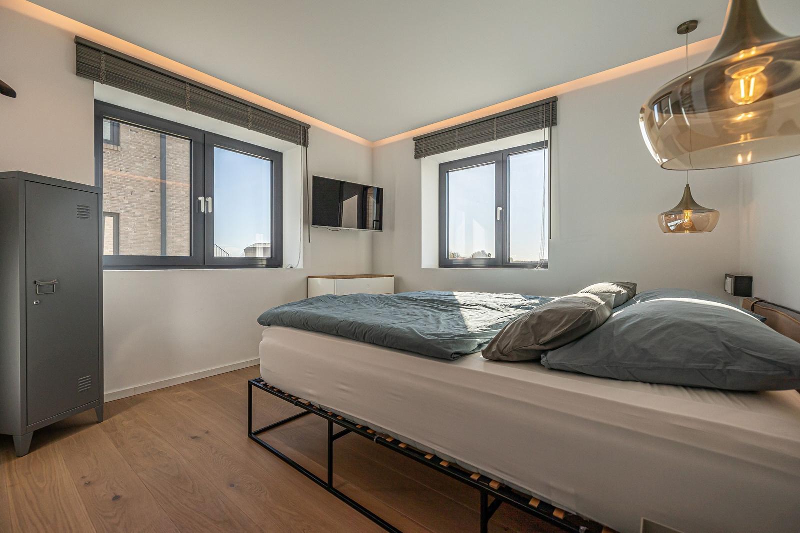 Schlafzimmer mit Bett, zwei Fenstern und Hängelampen.