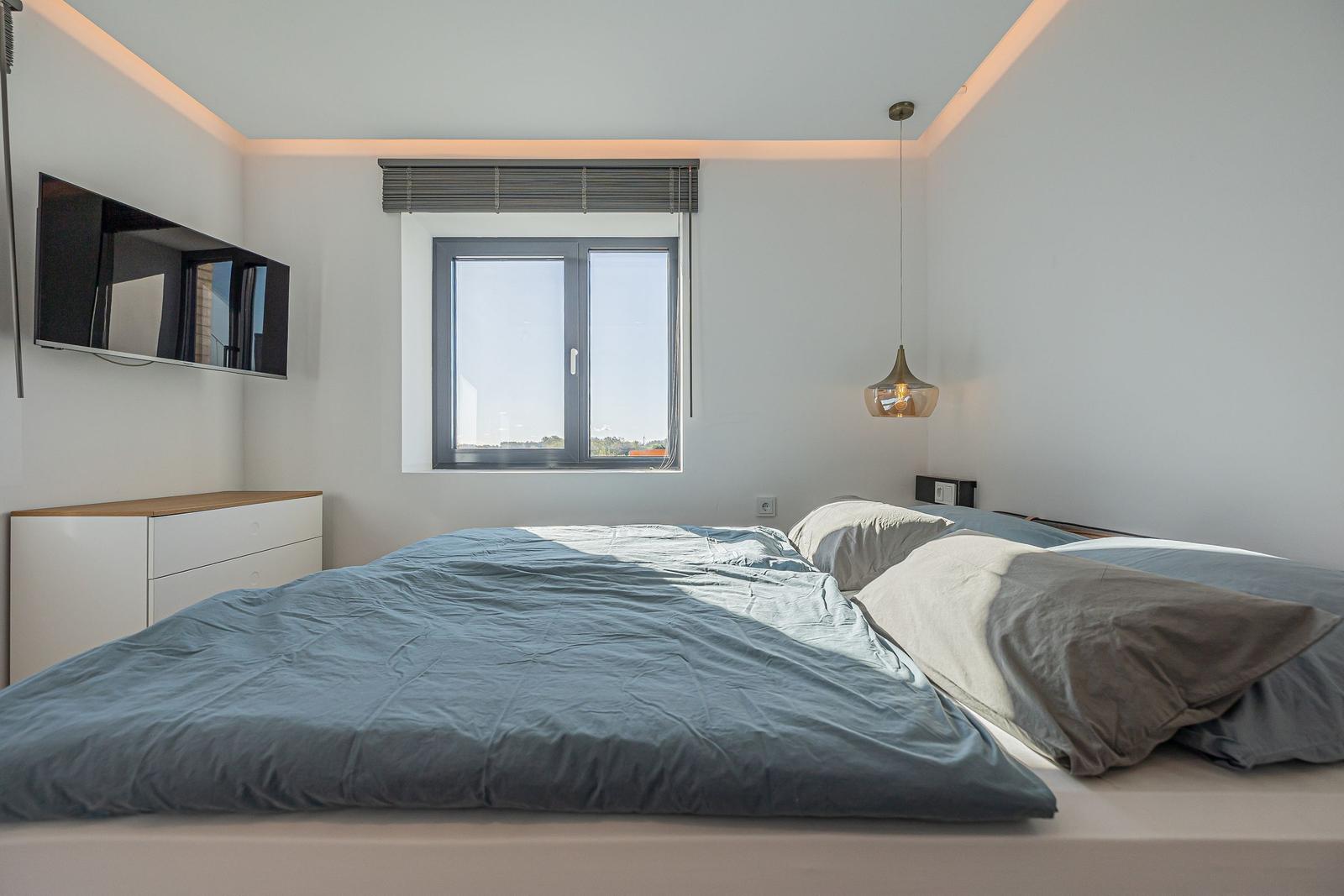 Schlafzimmer mit Bett, Fenster und TV an der Wand.